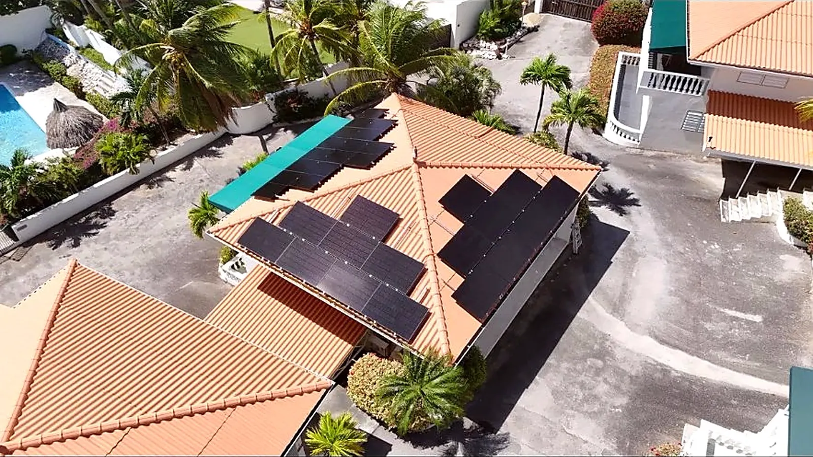 Zonnepanelen op de daken van een villa met palmbomen en zwembad op Curaçao