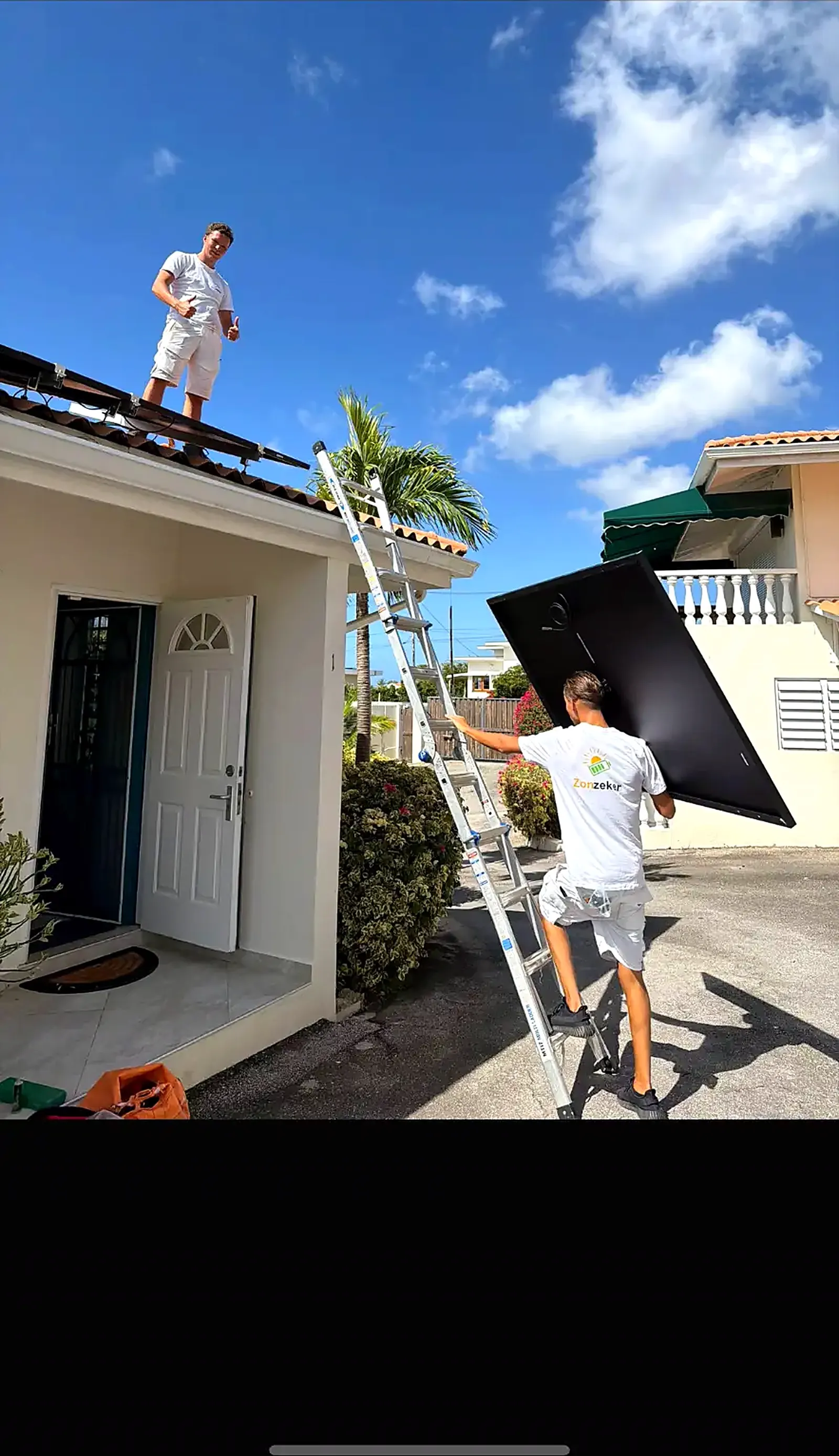 ZonZeker-monteurs met ladder en zonnepaneel bij een woning op Curaçao
